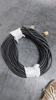 Full view of coiled black electrical extension cord secured with white tape on concrete floor.