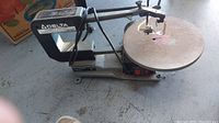 Full side view of the scroll saw showing the Delta logo, large round work table, and saw arm.