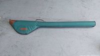 Full view of padded teal rod case with brown leather accents, laid flat on concrete floor