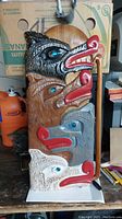 Full front view of the wooden carved art piece titled 'Wolf Pack' signed by Clayton Cal. Shows four vertically stacked wolf heads painted in black, brown, blue-gray, and white with red snouts and blue eyes.