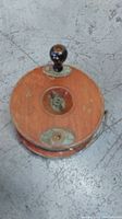 Photo of vintage Peetz style fishing reel top view showing wooden side plate, metal tension knob and black handle.