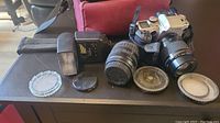 Photo showing camera body with attached lens, second zoom lens, external flash unit, lens caps, and red padded camera bag.