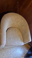 Top view showing rounded backrest and textured beige upholstery fabric with a leafy pattern.