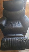 Black leather recliner chair showing seat and footrest extended, visible creasing in leather