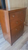 Full view of wooden dresser showing five drawers with round knobs, visible surface scratches and wear.