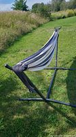 Vivere hammock with black metal frame stand and multi-colored striped fabric. Outdoor grassy setting. Shows entire hammock frame and cloth body attached.