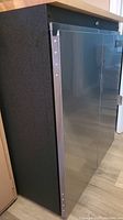 Side angle showing textured black steel body and stainless steel door with hinges and latch handle.
