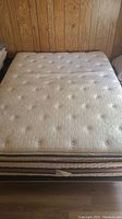 Top view of the queen size mattress showing white quilted surface with circular and floral stitched pattern, and striped side panels with some visible wear.