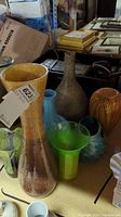 Overview of assorted art glass vases showing different shapes and color patterns including amber, green, blue and speckled beige.