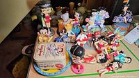 Full view of multiple Betty Boop figures in various poses and sizes arranged on a table, showing different decorations and styles.