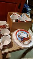 Cardboard box containing 13 white mugs with Campbell's Soup design in red and blue