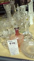 Group of crystal, milk glass, and pressed glass vases, cruet sets, and salt and pepper shakers shown on a table display.