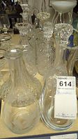 Photo showing a group of various glass and crystal decanters with some stoppers. Several decanters have etched or pressed glass designs.