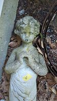 Close-up of the 31-inch tall cement garden figurine depicting a child with curly hair and hands near the chest, surface shows weathering and moss.