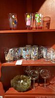 Shelf showing Disney character glasses including Mario, Princess Peach, and others, also clear glasses with etched designs and green glass ashtrays.