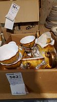 Box with 6 ceramic coffee cups with gold and brown glaze, scalloped edges, and tape residue visible on some cups
