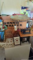 Wide shot of Jim Beam advertising figurine, empty bottle, miniature sewing machine, and Johnnie Walker crate in background