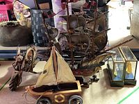 Photo showing a collection of model ships including a large ship, a smaller sailboat on wheels, a motorcycle figurine, and two glass cases with mini ships.