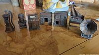 Seven vintage pencil sharpeners on a wooden surface, novelty shapes including water pump, bust, gas pump, mailbox, pipe organ, and gramophone horn.