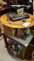 Wooden Glenlivet Whiskey circular bar sign on table with smaller items and steins below on shelf.