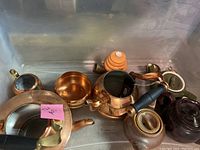 Overview of copper and ceramic tea pots along with accessories arranged in a metal bin.