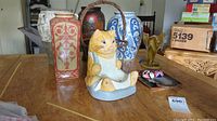 Overview photo of the lot showing all items on a table, including the cat figurine, basket, two tall vases, small masks, and the agate slice.