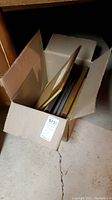 Box filled with several framed and unframed art prints showing condition and quantity.