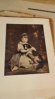 Unframed art print showing a young girl in period attire holding a dog, print is worn with visible stains and discoloration.