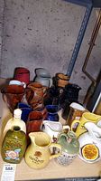 Wide shot showing multiple ceramic and porcelain whiskey decanters and pitchers in various shapes and colors on a table.