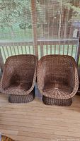 Pair of brown wicker chairs on wooden floor showing full front view and size.