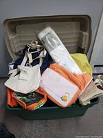 Various bags including tote bags, shoulder bags and rolled bags in different colors inside a green plastic container with lid.