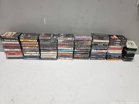 Stacks of approximately 51 cassette tapes arranged in rows showing spines and cases.