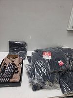 Photo of packaged light brown dress shirt with patterned tie and several navy blue uniform garments in plastic packaging