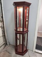 Front and side view of hexagonal wooden display shelf with glass panels and light inside.