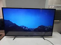 Front view of the Toshiba flatscreen TV powered on, displaying a mountainous night sky image, showing screen condition and design.