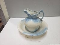 Porcelain jug placed inside porcelain bowl showing ornate scalloped spout, handle and blue cream color gradient with embossing.