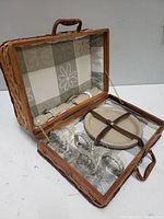 Wicker picnic basket open showing 4 beige plastic plates and 4 glass goblets with rope handles inside.