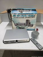 Photo shows silver main unit of home theatre sound system with remote control and original box.
