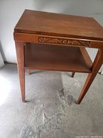 Front angled view showing tabletop, carved trim on apron, legs, and lower shelf