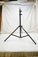 Full view of a black adjustable photo light stand with legs extended on a white background.
