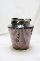 Photo of wrapped red pleated air filter with black top and clamp, isolated on white background.