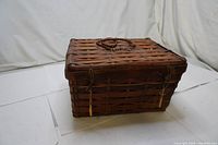 Closed vintage woven picnic basket made of wicker with leather straps for securing the lid.