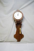 Front view of vintage battery powered wall clock showing round face with Roman numerals and faux wood design.