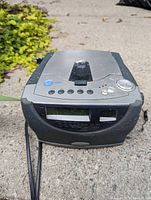 Sony CD radio alarm clock placed outdoors on a concrete surface showing front and clock face with control buttons and display under sunlight.