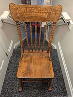Front view of antique wooden rocking chair showing carved backrest and turned spindles