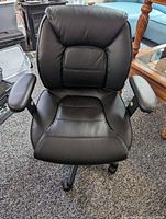 Front view of the black leather computer chair showing padded seat and backrest with cushioned armrests.