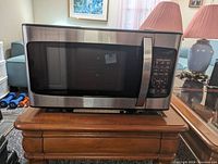 Hamilton Beach microwave oven closed, showing stainless steel body and front black digital control panel with buttons and display.
