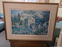 Framed painting showing a mill with a water wheel and garden in front.