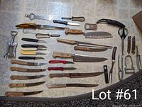 Photo shows a large variety of kitchen cutting tools including knives, peelers, kitchen shears, corkscrew, bottle openers, nutcracker and sharpener laid out on a tiled surface.