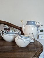 Photo of three tea set pieces including teapot, sugar bowl, and creamer on wooden surface.